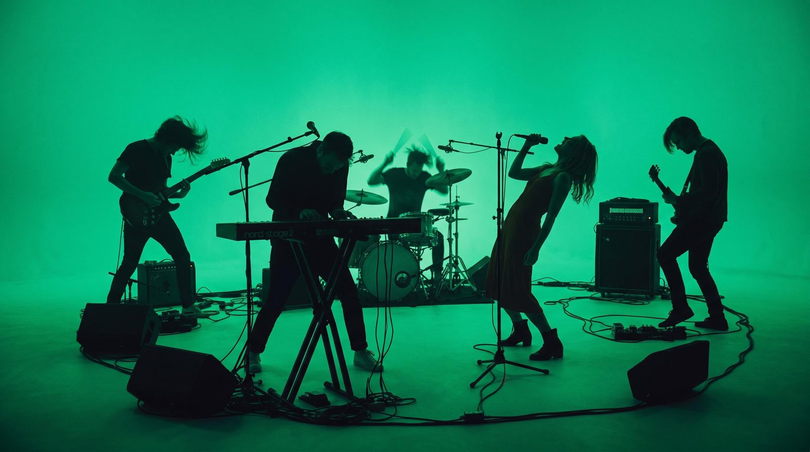 Music-video frame concept of a five-piece band silhouetted against vivid green stage lighting.