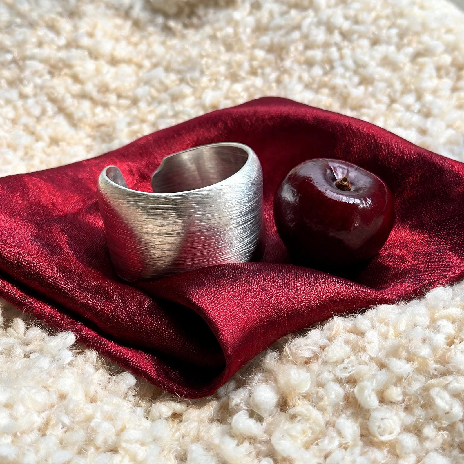 Brushed silver cuff and a dark cherry on burgundy silk and ivory wool, generated at 3072 by 3072 pixels with Seedream 5.0 Lite.