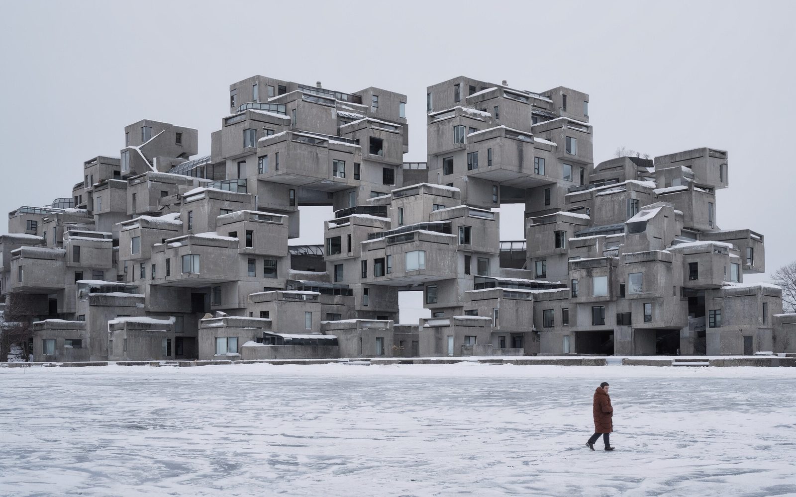 Habitat 67 in Montreal under snow, seen across the frozen river with one figure in a rust-red parka