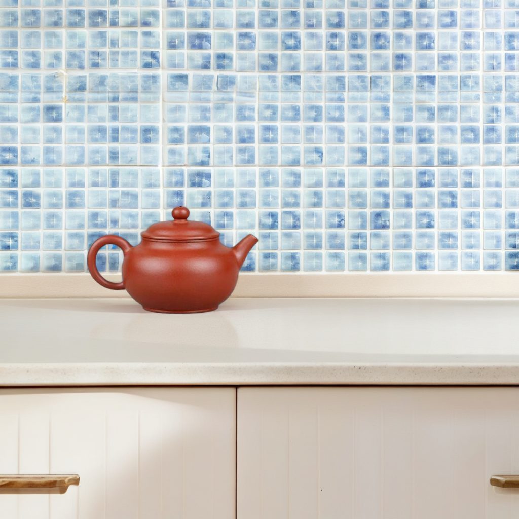 Coral-red teapot placed left of center on an ivory counter against pale blue tiles.