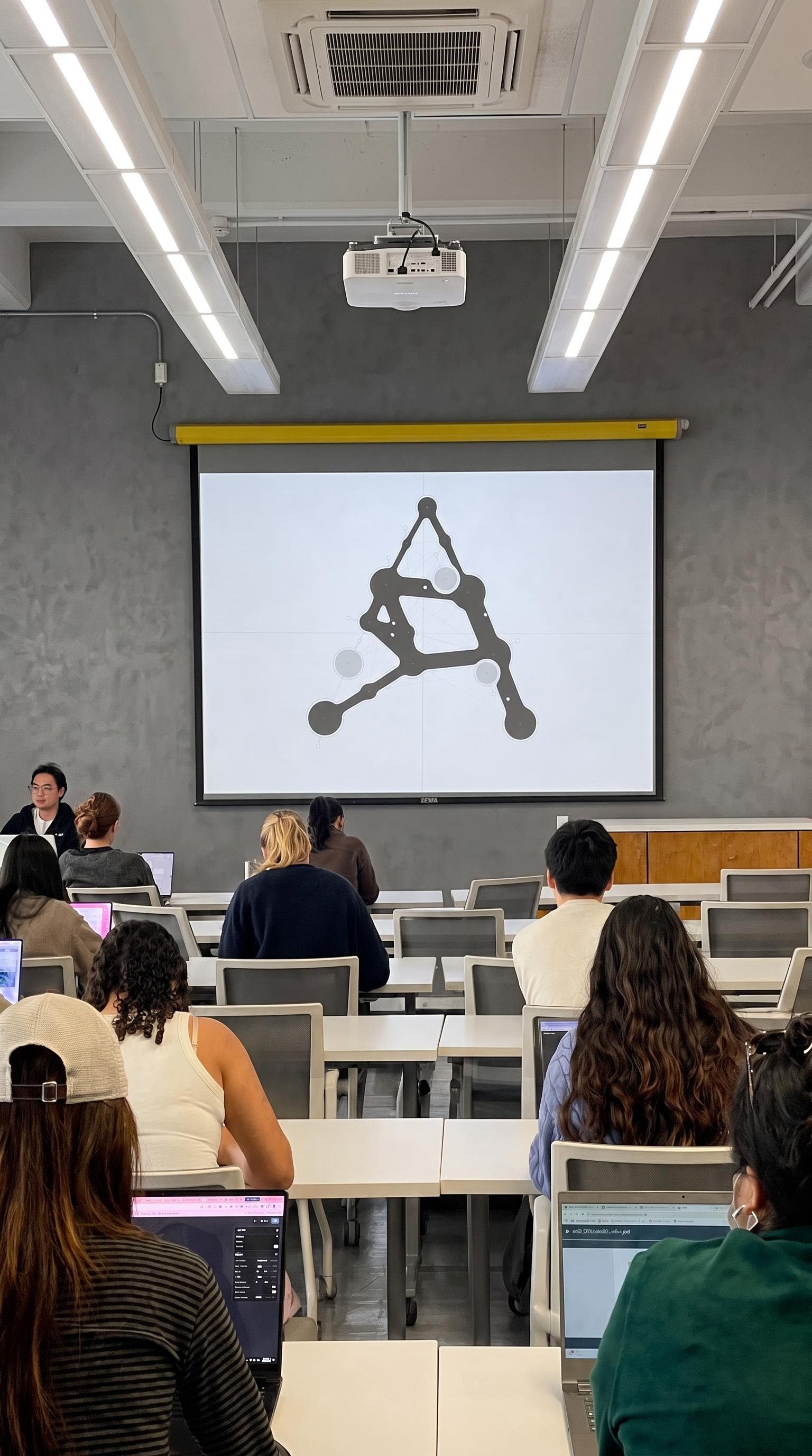 Presentation concept showing an audience facing a projected abstract letterform diagram in a classroom.