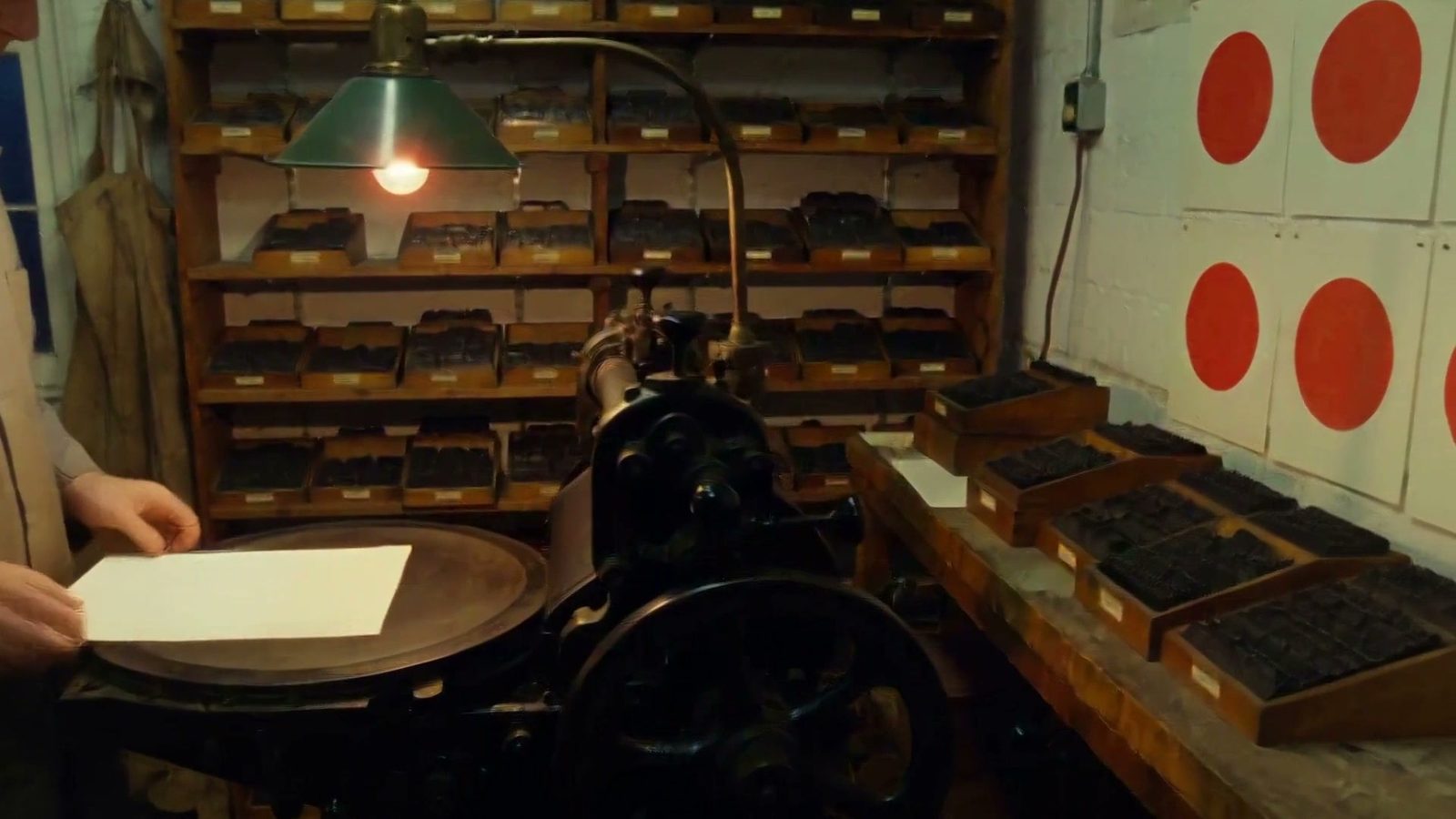 A night letterpress shop under a green lamp, widened to 16:9 by MiniMax H3 Reframe, which added a canvas apron on the left and red-circle prints on the wall.