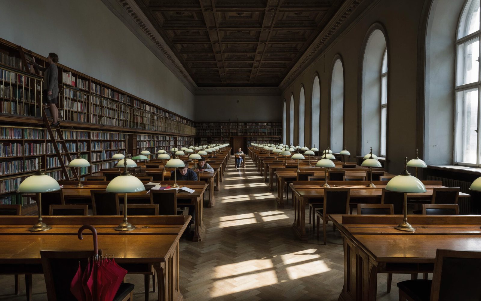 Long 1930s library reading room with green-shaded lamps, a librarian on a ladder and a red umbrella on a chair