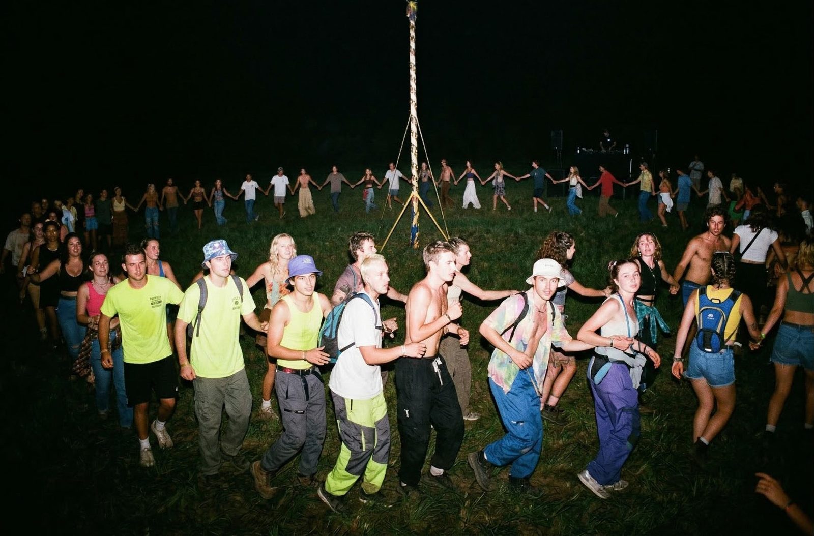 Nighttime scene concept of a crowd dancing around a decorated pole under bright lighting.