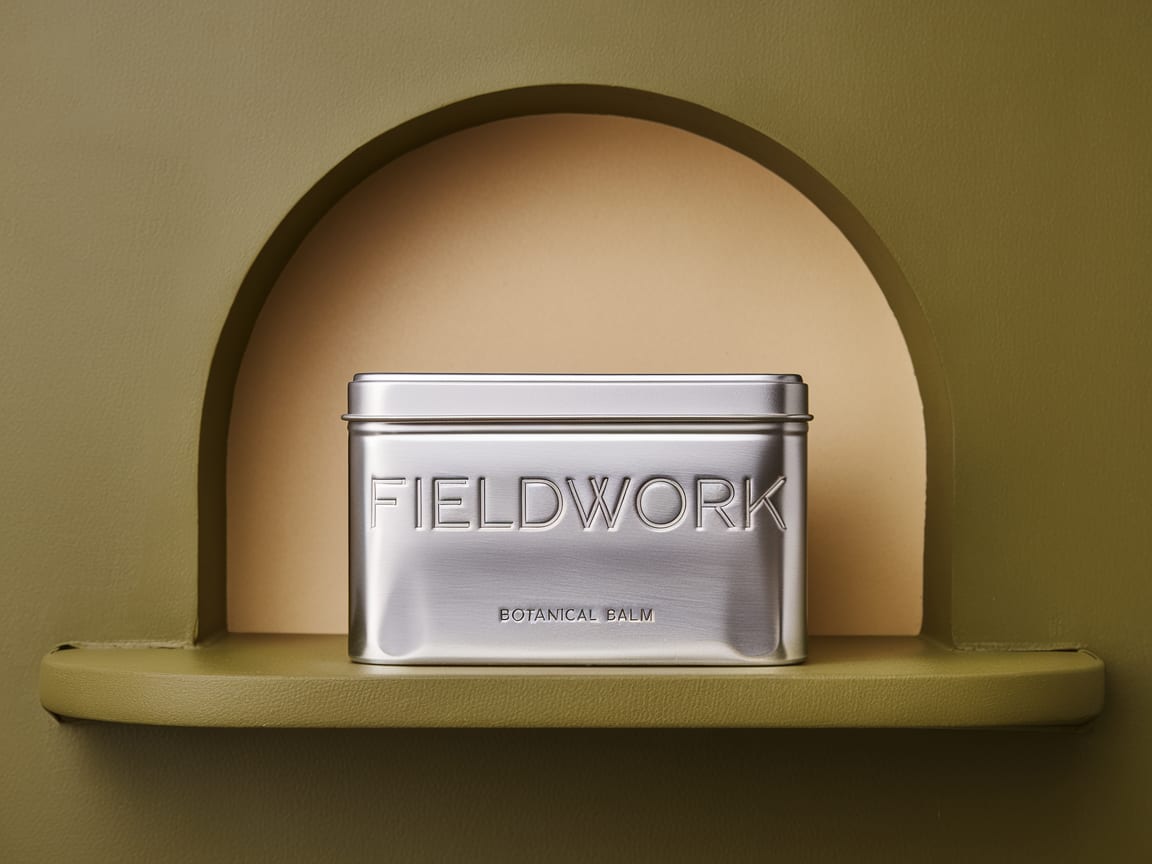 Silver FIELDWORK botanical balm tin displayed in an olive architectural niche.