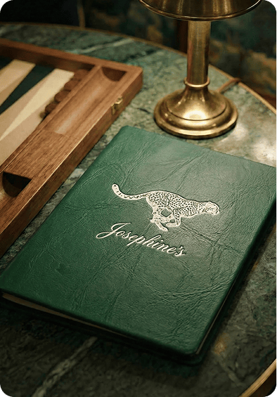 A dark green leather bound menu with an embossed cheetah in a dim lit restaurant
