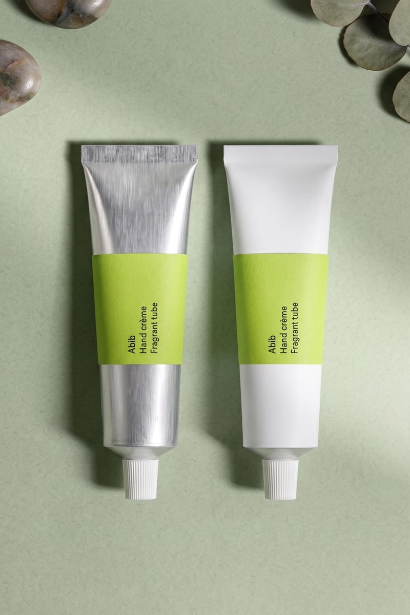 Skincare packaging concept with silver and white tubes, lime-green labels and metallic props on a pale green surface.