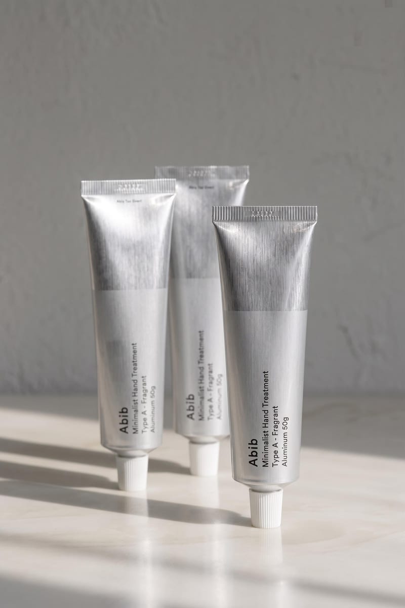Still product concept of three silver skincare tubes on a light surface with soft directional shadows.