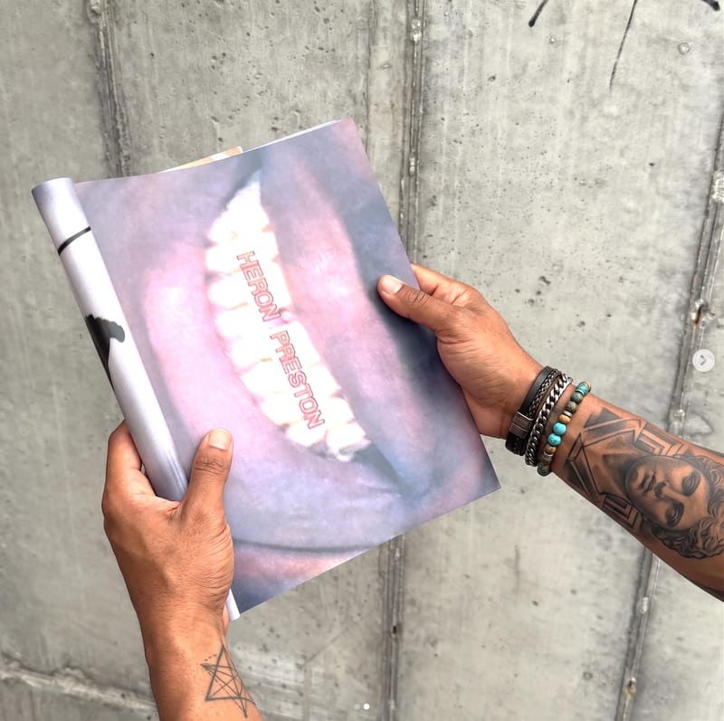 Social-content concept of tattooed hands holding a printed artwork with a close-up teeth illustration against a concrete wall.