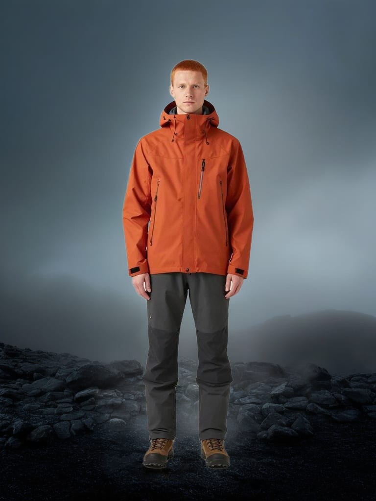 Burnt-orange technical outerwear staged among dark volcanic rocks and gray mist.