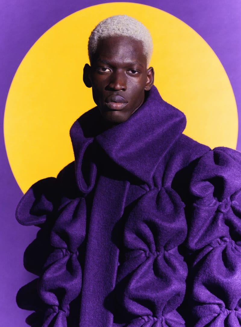 Fashion portrait with a purple sculptural coat and bold yellow color blocking.