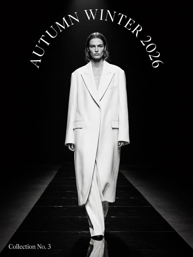 Black and white runway photo of a model in an oversized white coat under an arc of thin serif text reading AUTUMN WINTER 2026