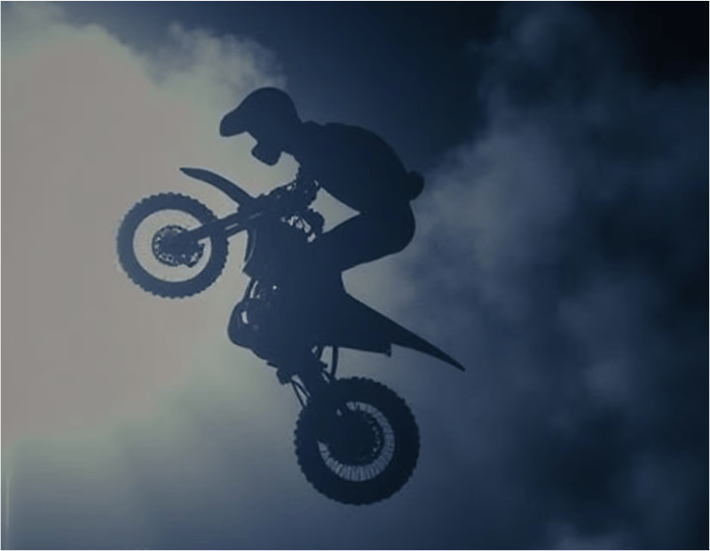 Silhouette of a rider lifting a motorcycle against a smoky blue background.