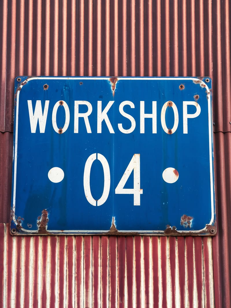 Weathered blue WORKSHOP 04 sign on a rust-red corrugated wall.