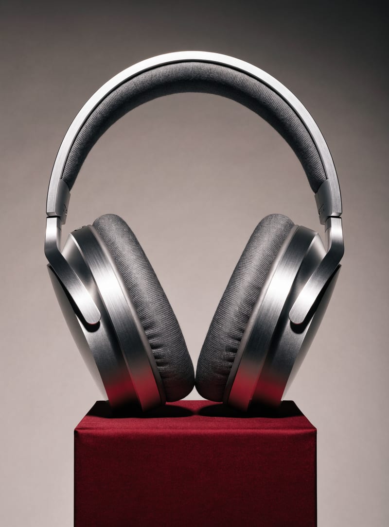 Complete brushed aluminum headphones with detailed ear cushions on a burgundy pedestal.