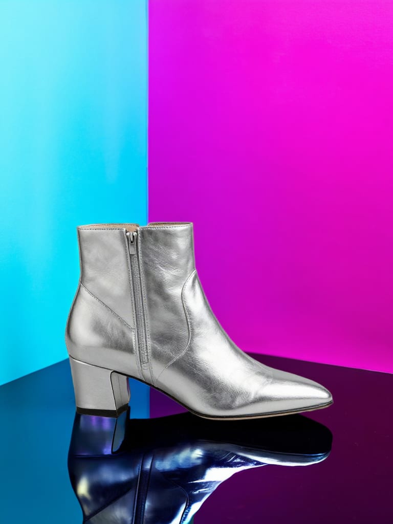 Silver ankle boot on a reflective platform against saturated cyan and magenta.